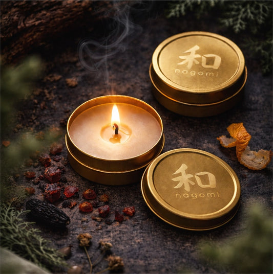 Lit Nagomi Dragon’s Whisper mini-tin candles arranged outdoors with oranges, cedarwood shavings, and tonka beans