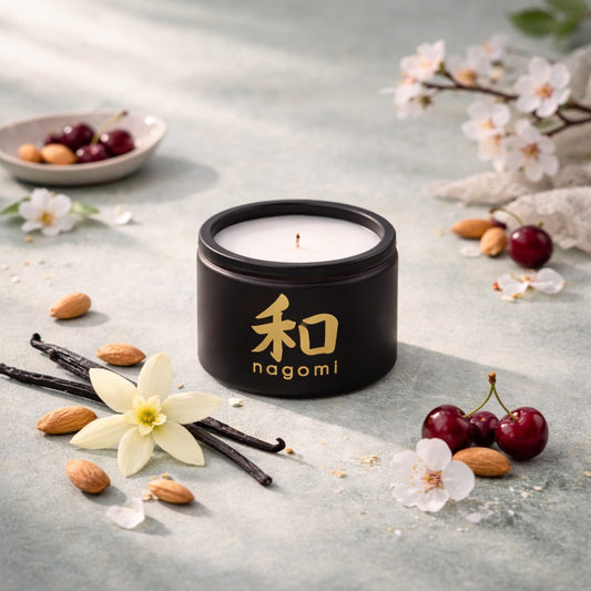 Four-ounce Nagomi Aromatic Journey candle in a black glass jar on a neutral background with cherries, almonds, and vanilla beans.
