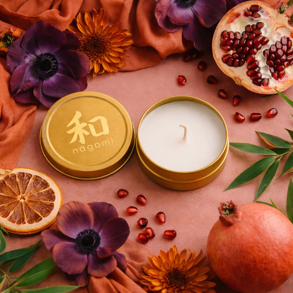 Mini-Tin Nagomi Eternal Ascent Candle in a gold tin, on a neutral background with oranges, plums and bamboo