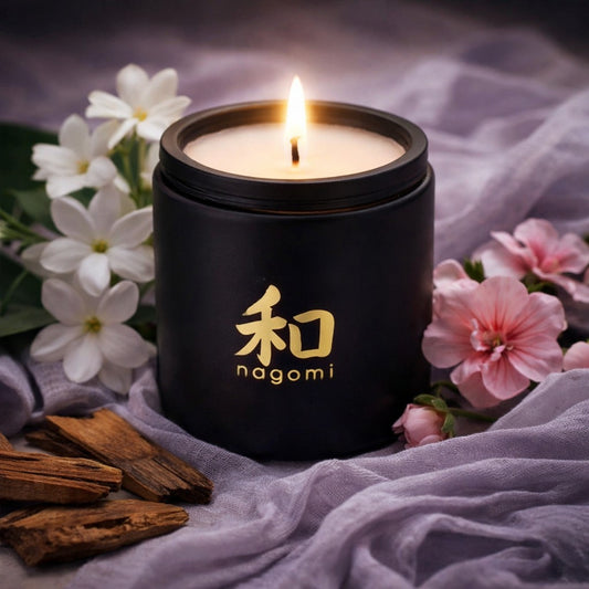 Nagomi Mystic Alchemy 12 oz candle in a black jar with Jasmine, geranium and teakwood in the background