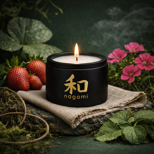 Four-ounce Nagomi Tenacious Bloom candle in a black glass jar, lit, on a neutral background with strawberries, geraniums, and moss.