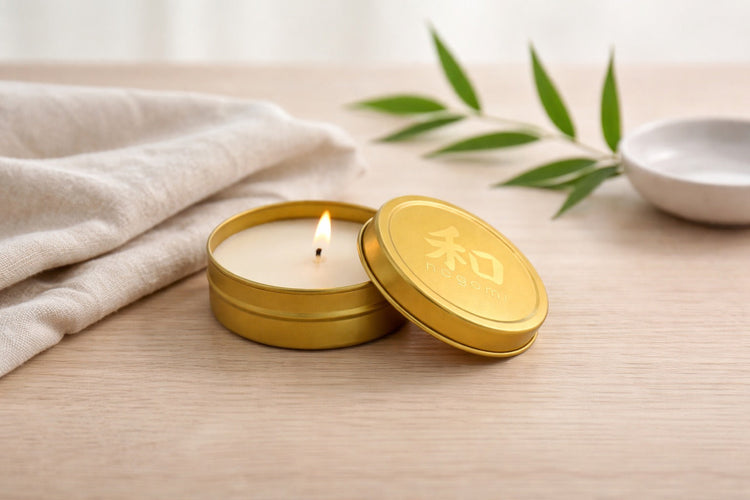 Nagomi mini tin candle with lit flame on wooden surface with folded cloth and bamboo