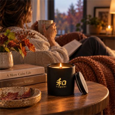 An Autumn's Sigh candle lit beside a woman relaxing with a book and warm drink on a fall evening
