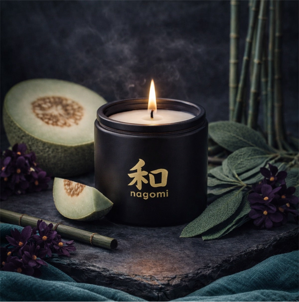 12 oz Close-up of a lit Nagomi candle flame with casaba melon, bamboo, and dark violet flowers nearby