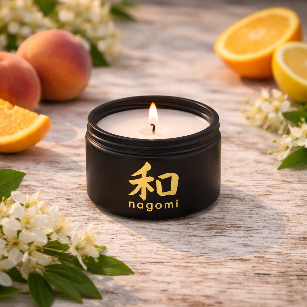 4 oz. Nagomi Citrus Vitality candle glowing on a sandy surface with fresh orange slices, peaches, and jasmine blooms
