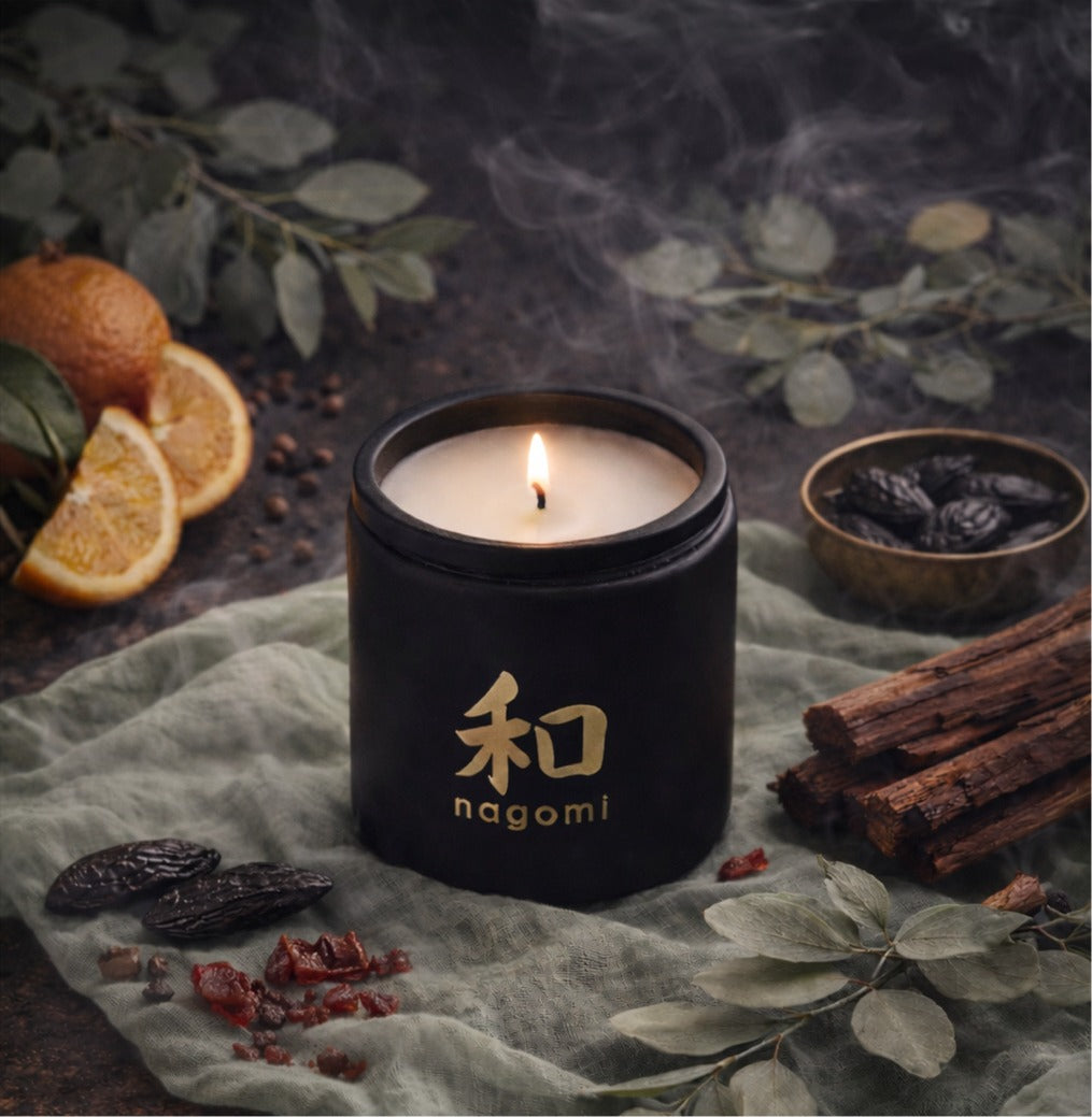 Close-up of a lit 12 oz Nagomi candle flame with oranges, cedarwood shavings, and tonka beans nearby