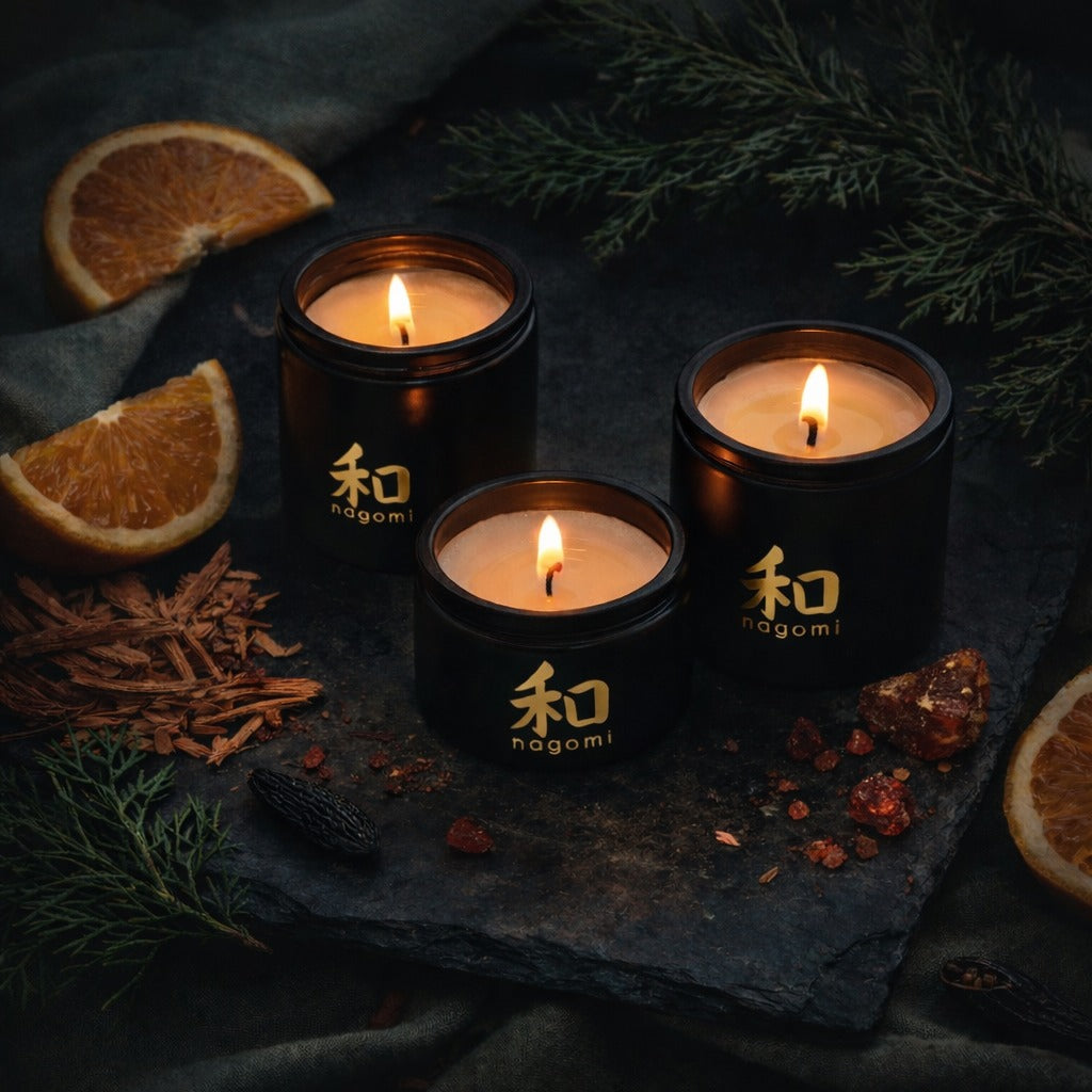 Lit Nagomi Dragon’s Whisper candles in black glass jars in a forest setting with oranges, cedarwood shavings, and tonka beans