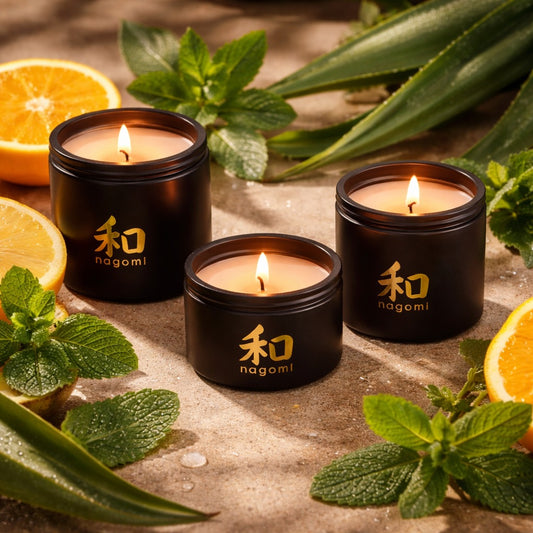 Three lit Nagomi Mikan Dreams candles in black glass jars, surrounded by orange slices, mint leaves, and agave stalks
