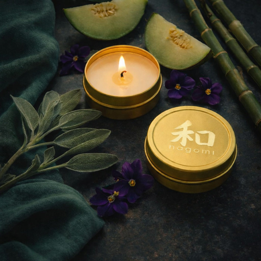 Lit Nagomi Woodland Dream mini-tin candles arranged on stone plates with casaba melon, bamboo, and dark violet flowers