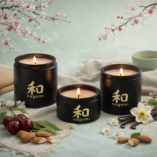 Three Nagomi Aromatic Journey candles in black glass jars with lit flames on a neutral background with cherries, almonds, and vanilla beans.