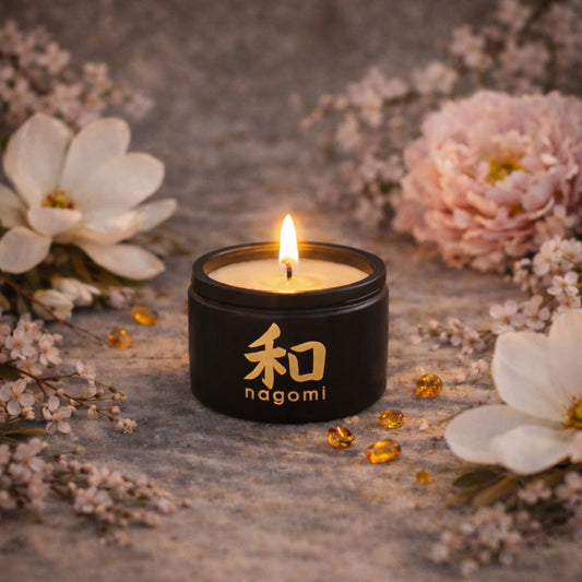 4 oz Nagomi Blossom Odori candle glowing on a sandy surface with cherry blossoms, magnolia blooms, and amber accents