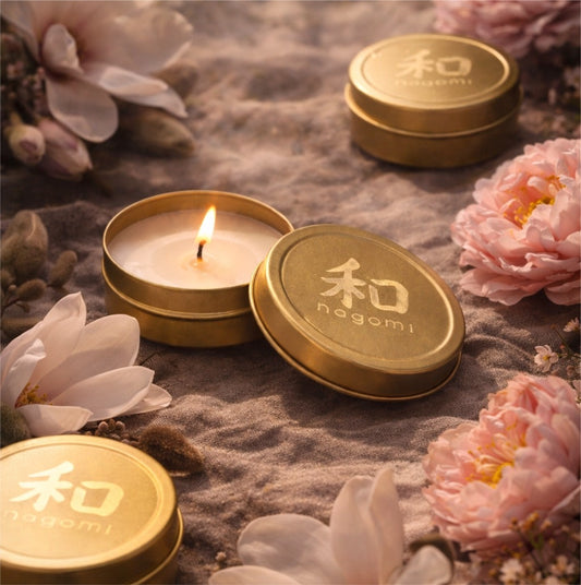 Lit Nagomi Blossom Odori mini-tin candles arranged on sand with cherry blossoms, magnolia flowers, and amber