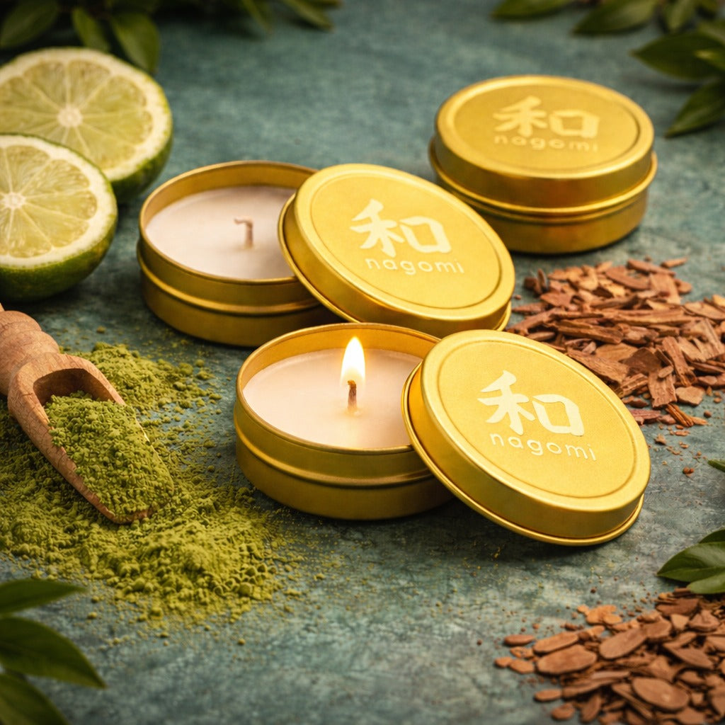 Nagomi Aromatic Journey mini-tin candles in gold metallic containers, lit, on a neutral background with bergamot, matcha, and sandalwood.