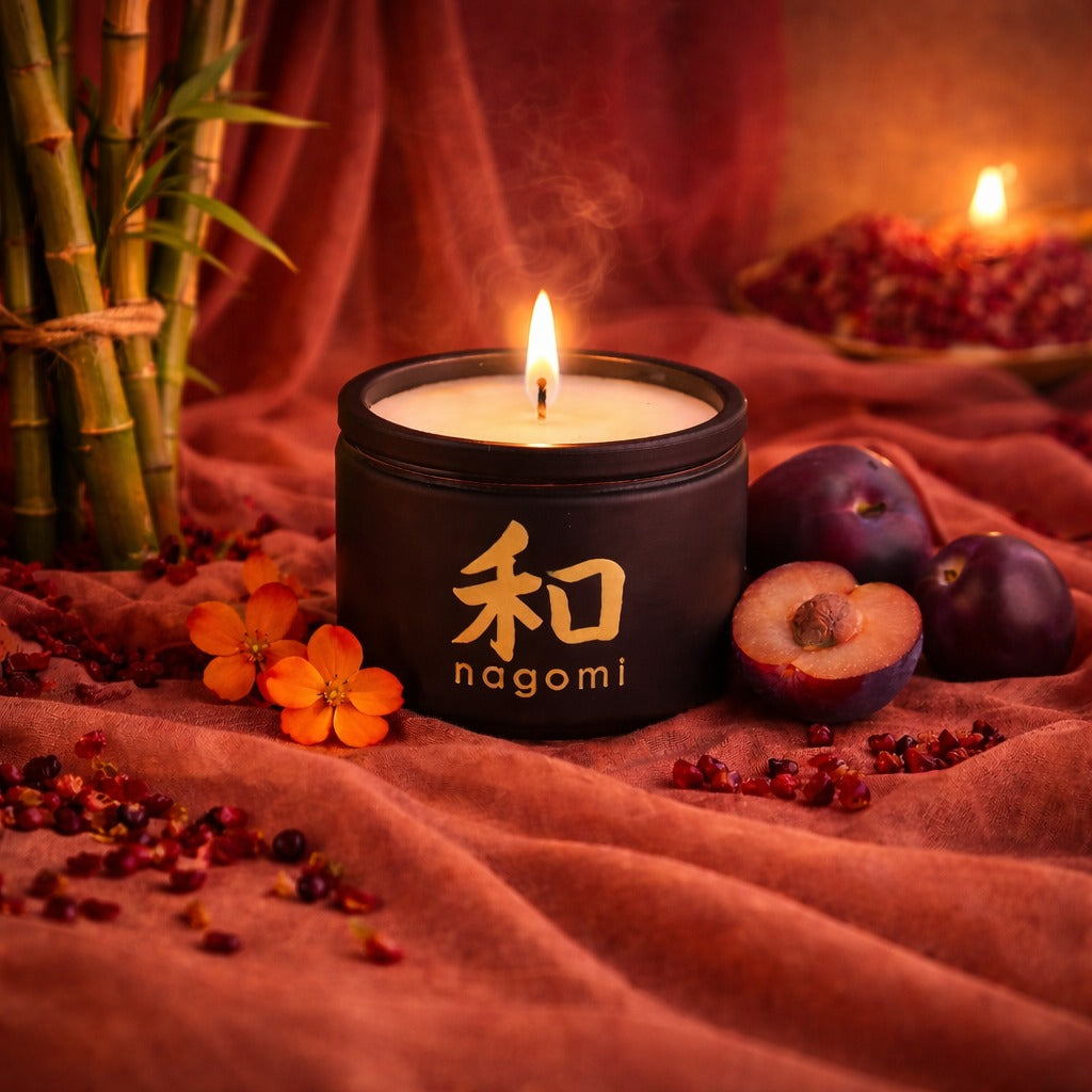 Four-ounce Nagomi Eternal Ascent Candle in a black glass jar, lit, on a neutral background with oranges, plums and bamboo