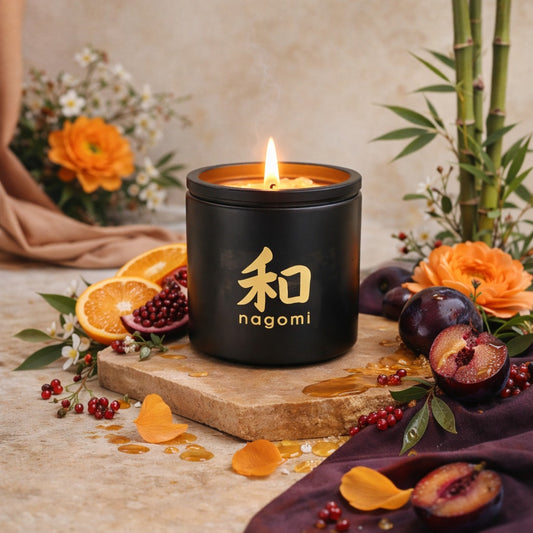 Eight-ounce Nagomi Eternal Ascent Candle in a black glass jar, lit, on a neutral background with oranges, plums and bamboo