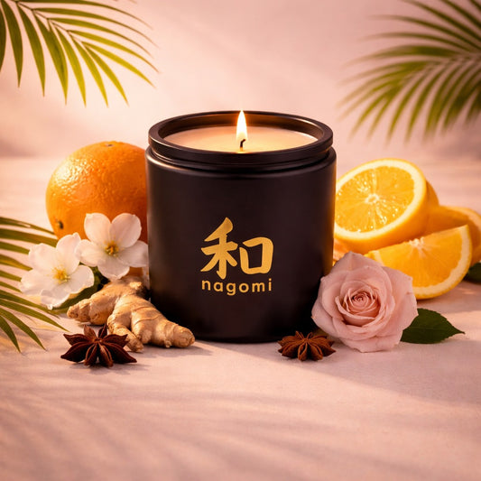 A twelve-ounce Nagomi Lahain's Aure candle in a black glass jar, lit, on a neutral background with citrus fruit, jasmine, roses and spices