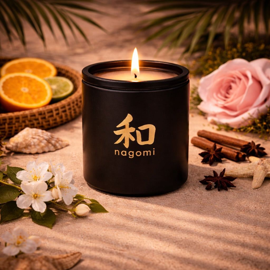 An eight-ounce Nagomi Lahain's Aure candle in a black glass jar, lit, on a neutral background with citrus fruit, jasmine, roses and spices