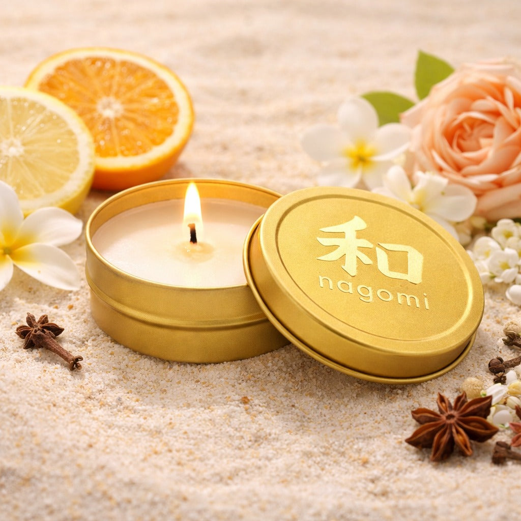 A mini-tin Nagomi Lahain's Aure candle in a gold tin, lit, on a neutral background with citrus fruit, jasmine, roses and spices