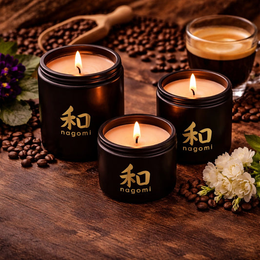 Three Nagomi Mindful Brew candles in black glass jars, lit, on a neutral background with fruit, coffee, and african violets