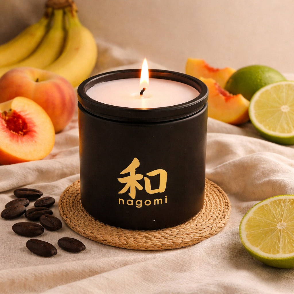 Twelve-ounce Nagomi Peach Serenity candle in black glass jar, lit, on a neutral background with lime, banana, peaches and tonka bean
