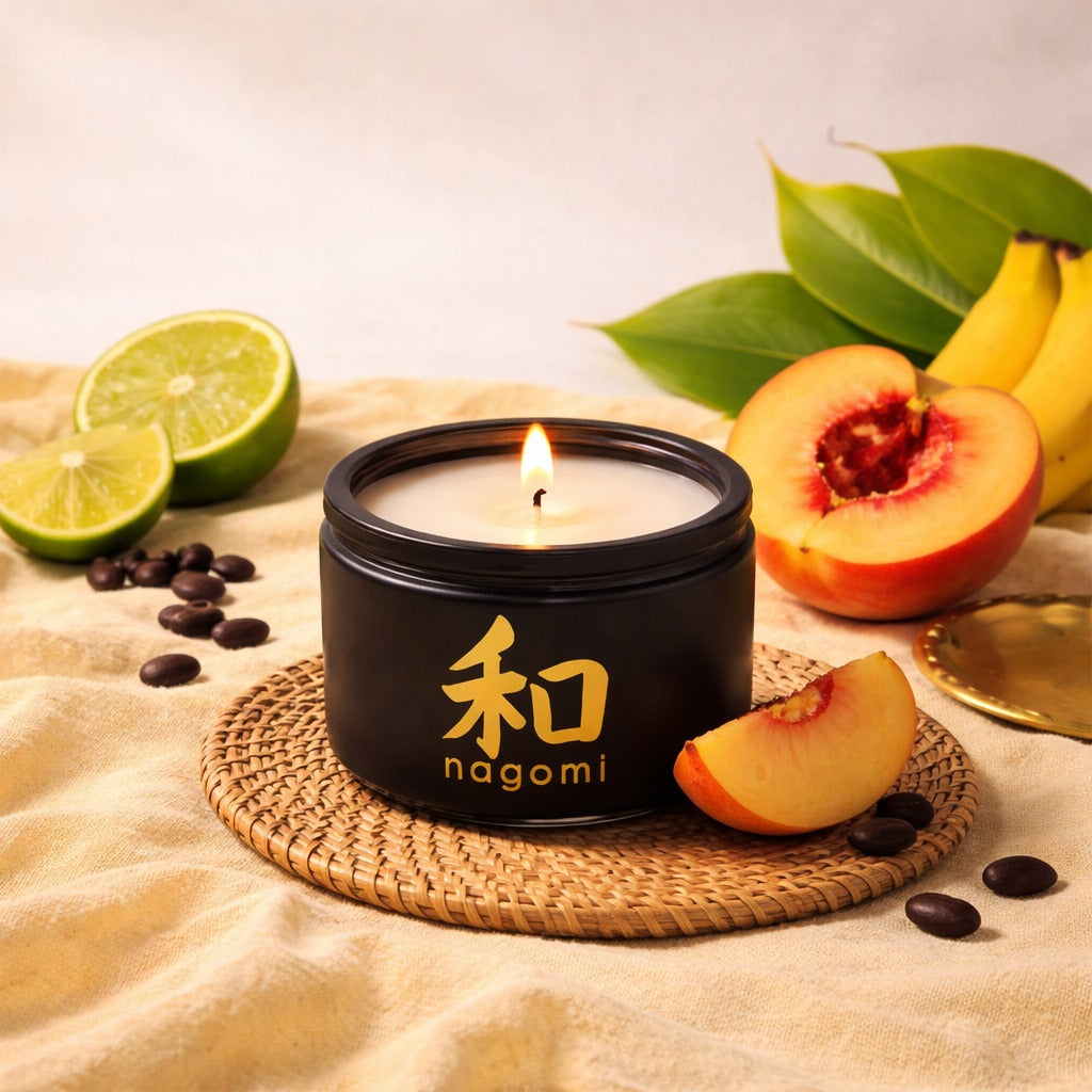 Four-ounce Nagomi Peach Serenity candle in black glass jar, lit, on a neutral background with lime, banana, peaches and tonka bean