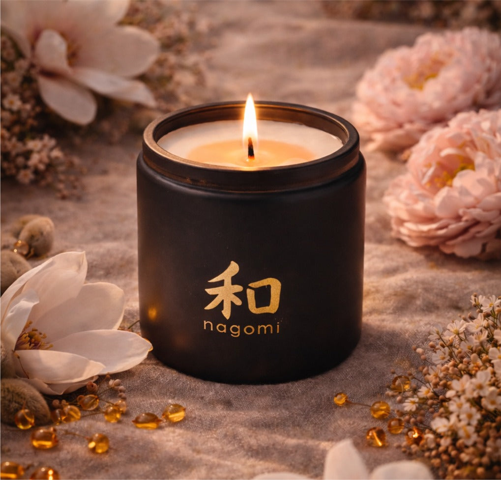 Close-up of a lit 12 oz Nagomi candle flame with cherry blossoms, magnolia petals, and amber nearby
